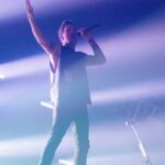 A musician performing on stage with a microphone, surrounded by dramatic lighting and smoke effects.